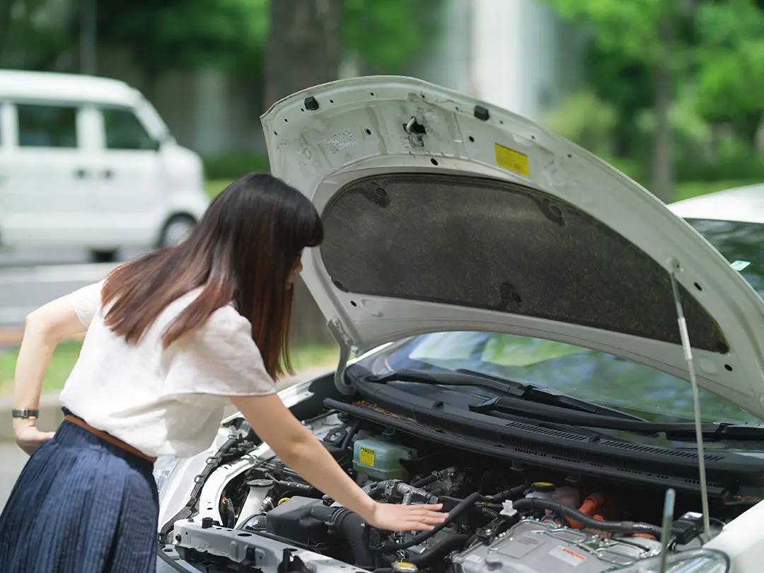 エンジントラブルに見舞われエンジンルームを覗く女性カーオーナー